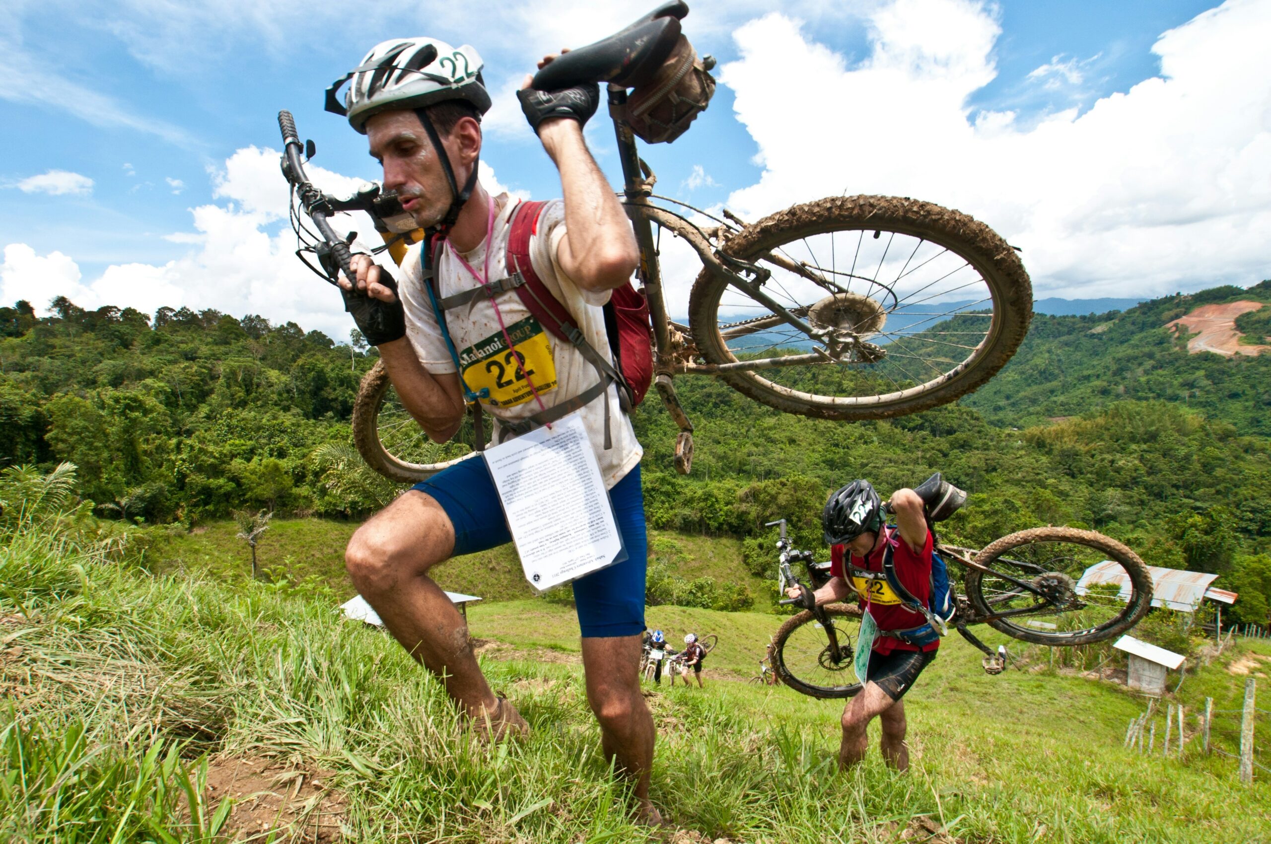 A close-up shot of essential mountain biking gear laid out neatly on grass, including helmets, gloves, hydration packs, and tools.