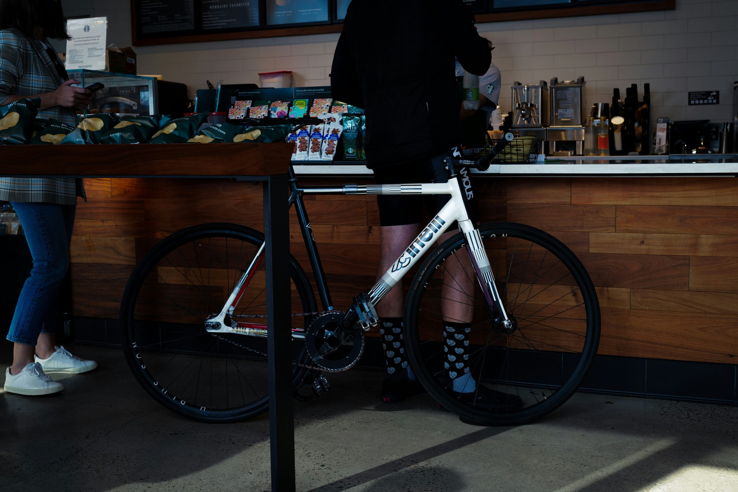 A young cyclist seated at an open-air café table sipping coffee with his helmet resting beside him.