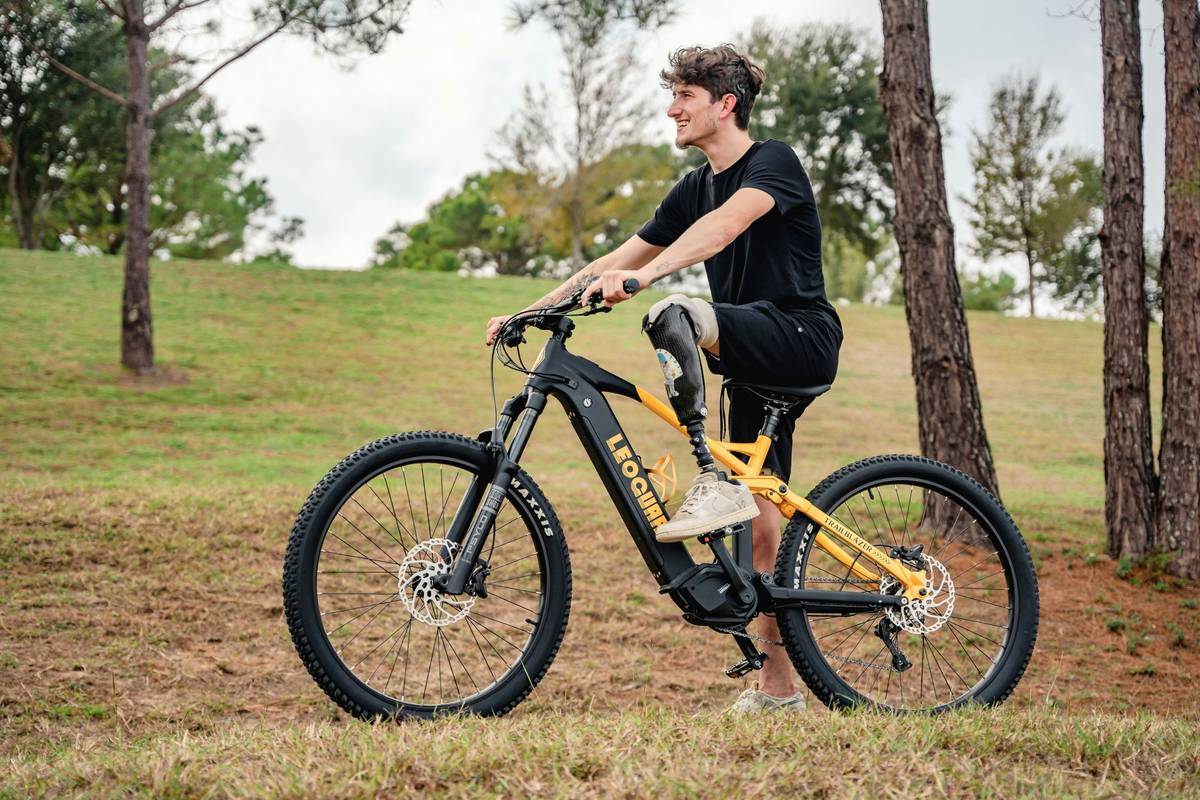 A cyclist on an e-bike riding along a scenic coastal path with mountains in the background