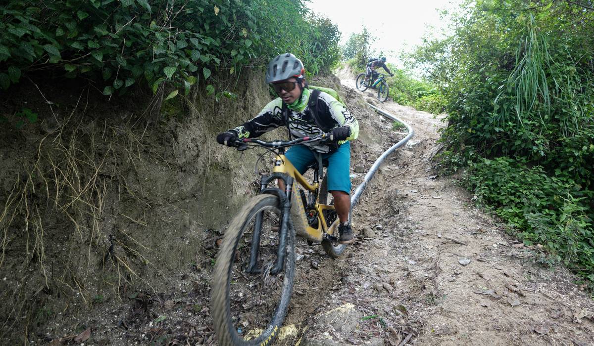 A rugged ebike parked on a rocky trail surrounded by lush greenery